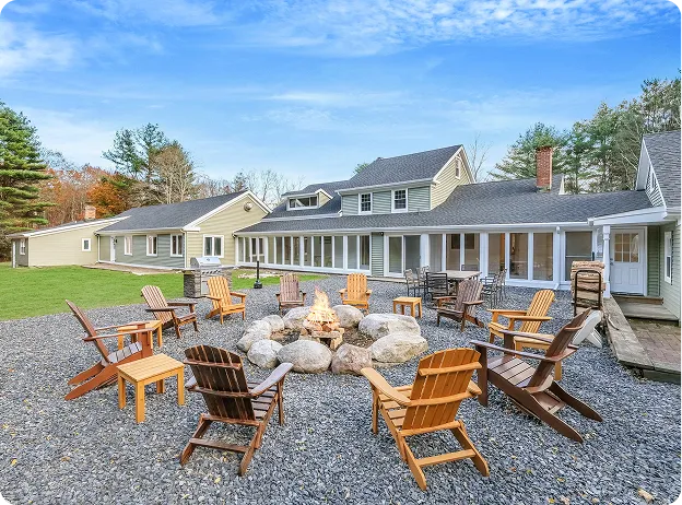An Image of an Outdoor fire pit with Adirondack chairs in front of a large house