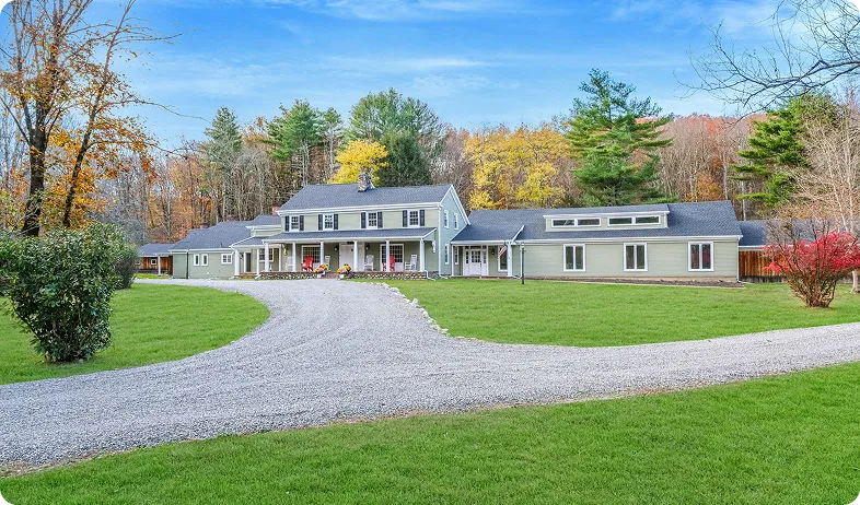 An Image of a Large green house with gravel driveway and autumn trees