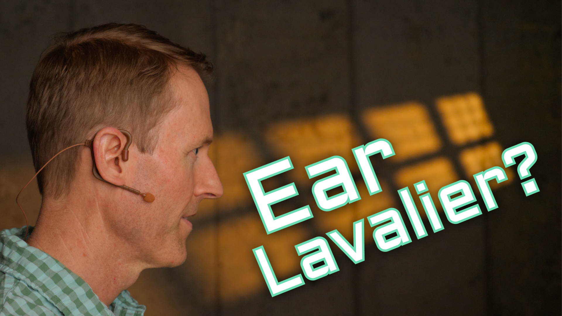 Curtis faces to the side against a lit concrete backdrop and shows how simple it is to wear and use the PointSource Audio Embrace on-ear lavalier mic.