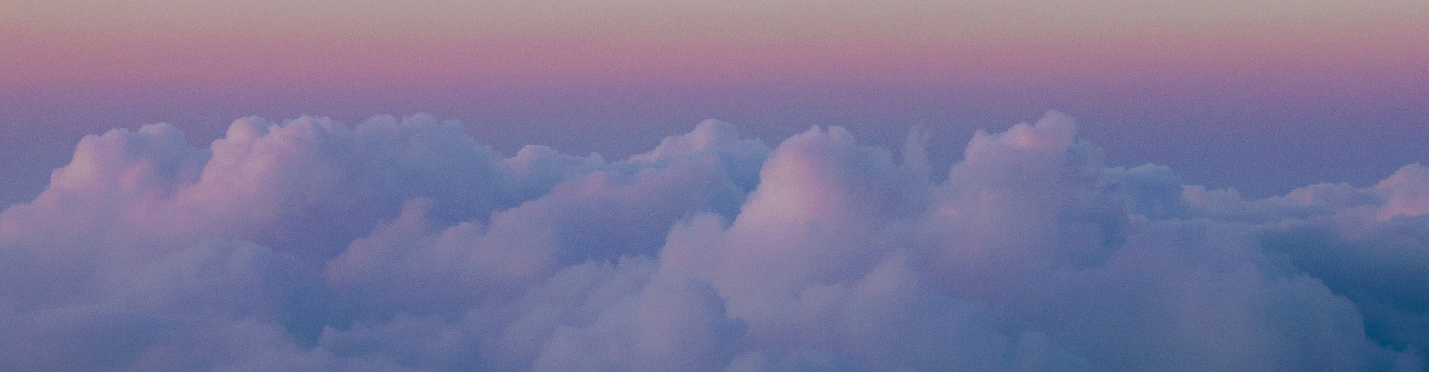 Fluffy clouds bathed in soft pink and purple hues stretch across the horizon at sunset, creating a serene and dreamy atmosphere.