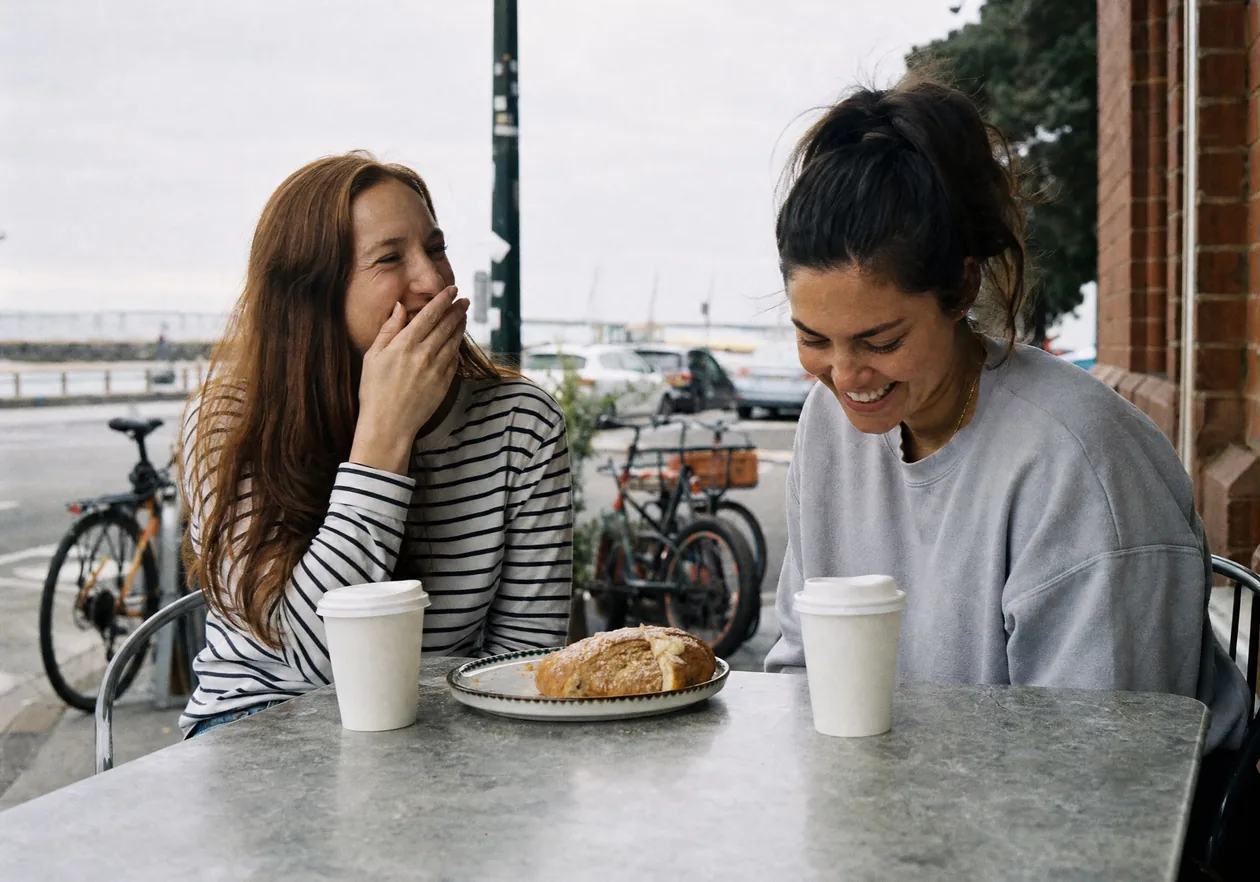 Two friends laughing over coffee at a cafe