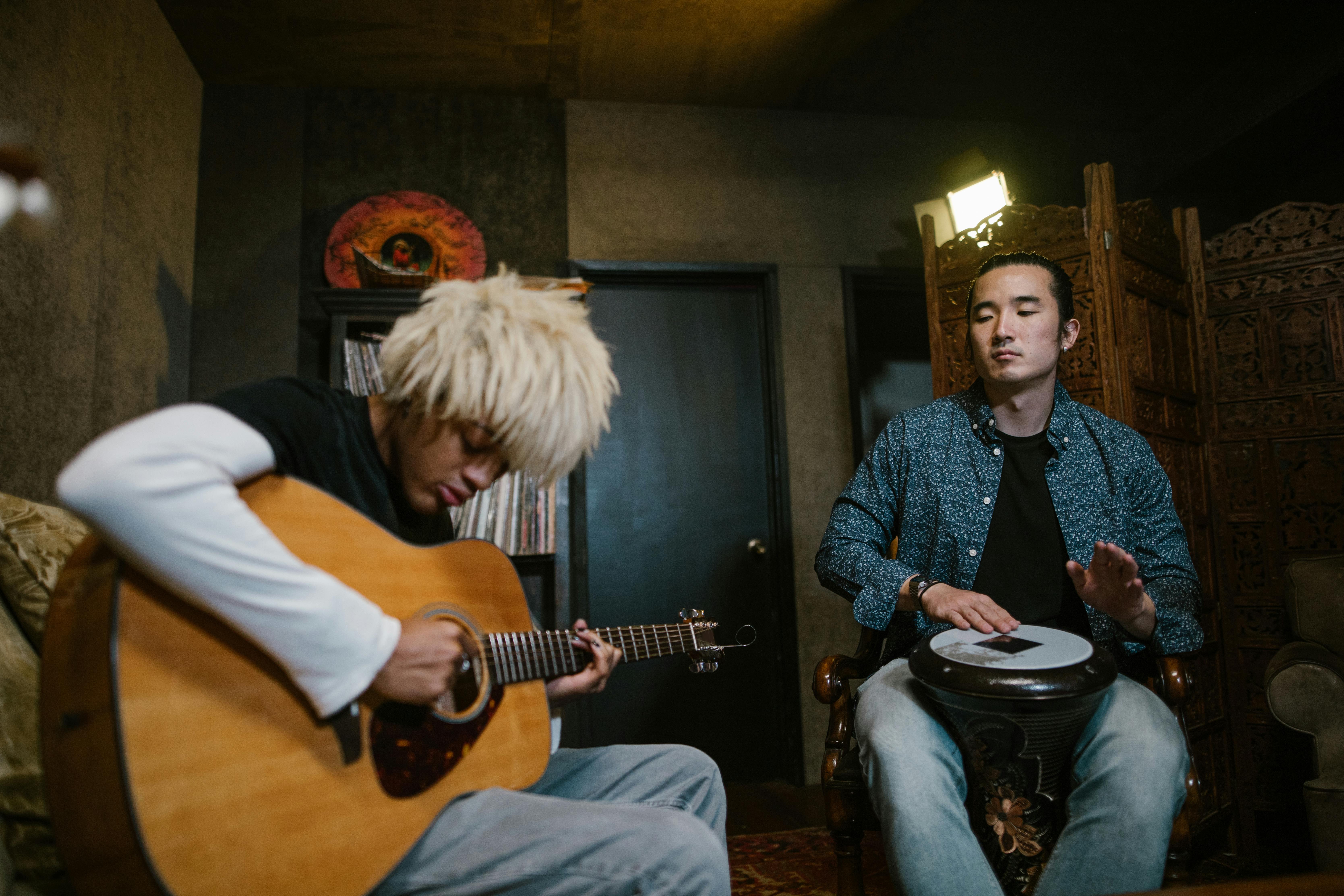 Two musicians immersed in a jam band session, one playing an acoustic guitar while the other keeps rhythm on a djembe drum, creating a soulful and intimate musical experience in a cozy indoor setting. 