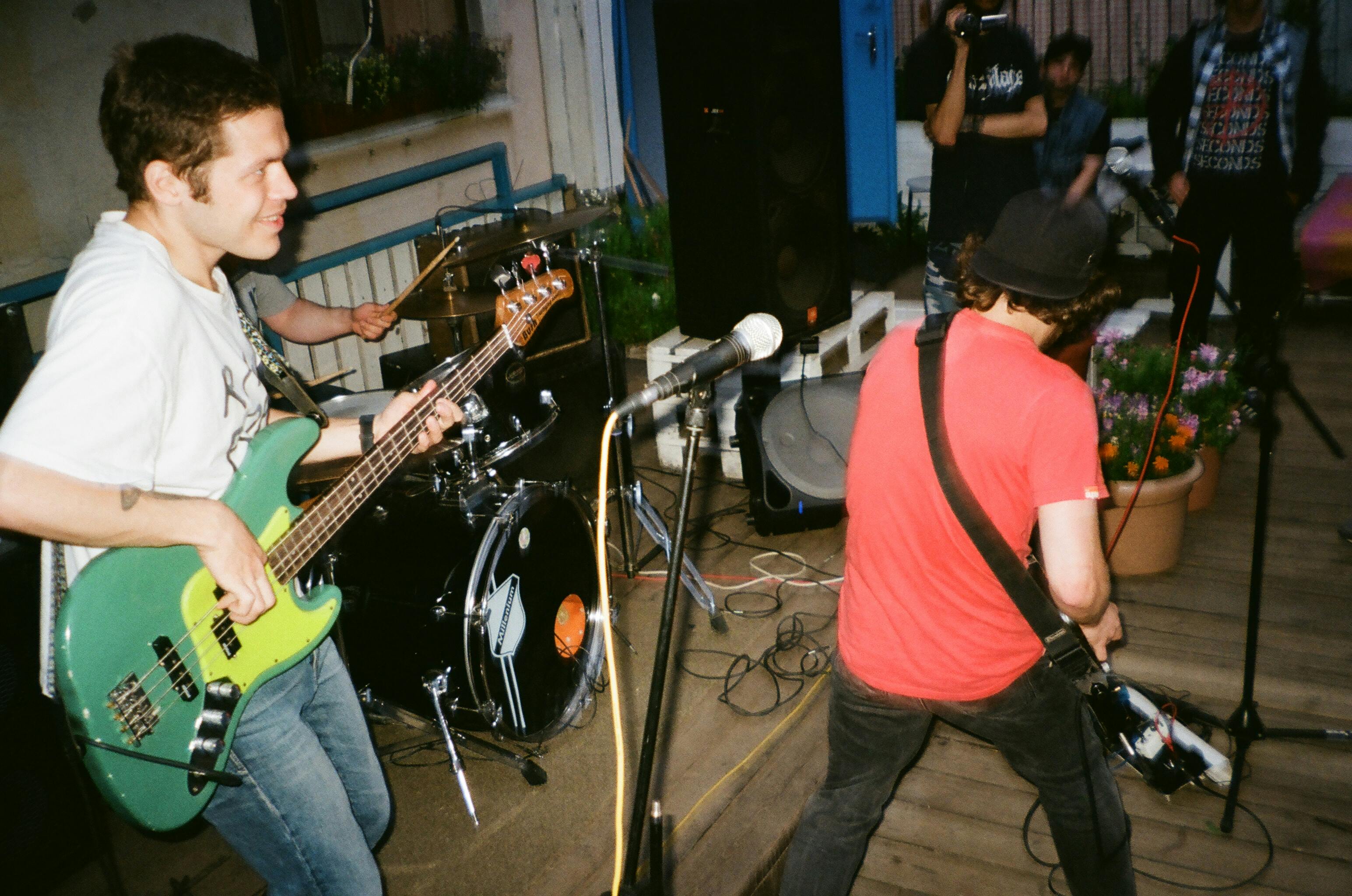 Two musicians performing live on stage, one playing a green bass guitar and the other playing an electric guitar, showcasing the energy and synergy of a great guitar partner duo in a vibrant music scene. 