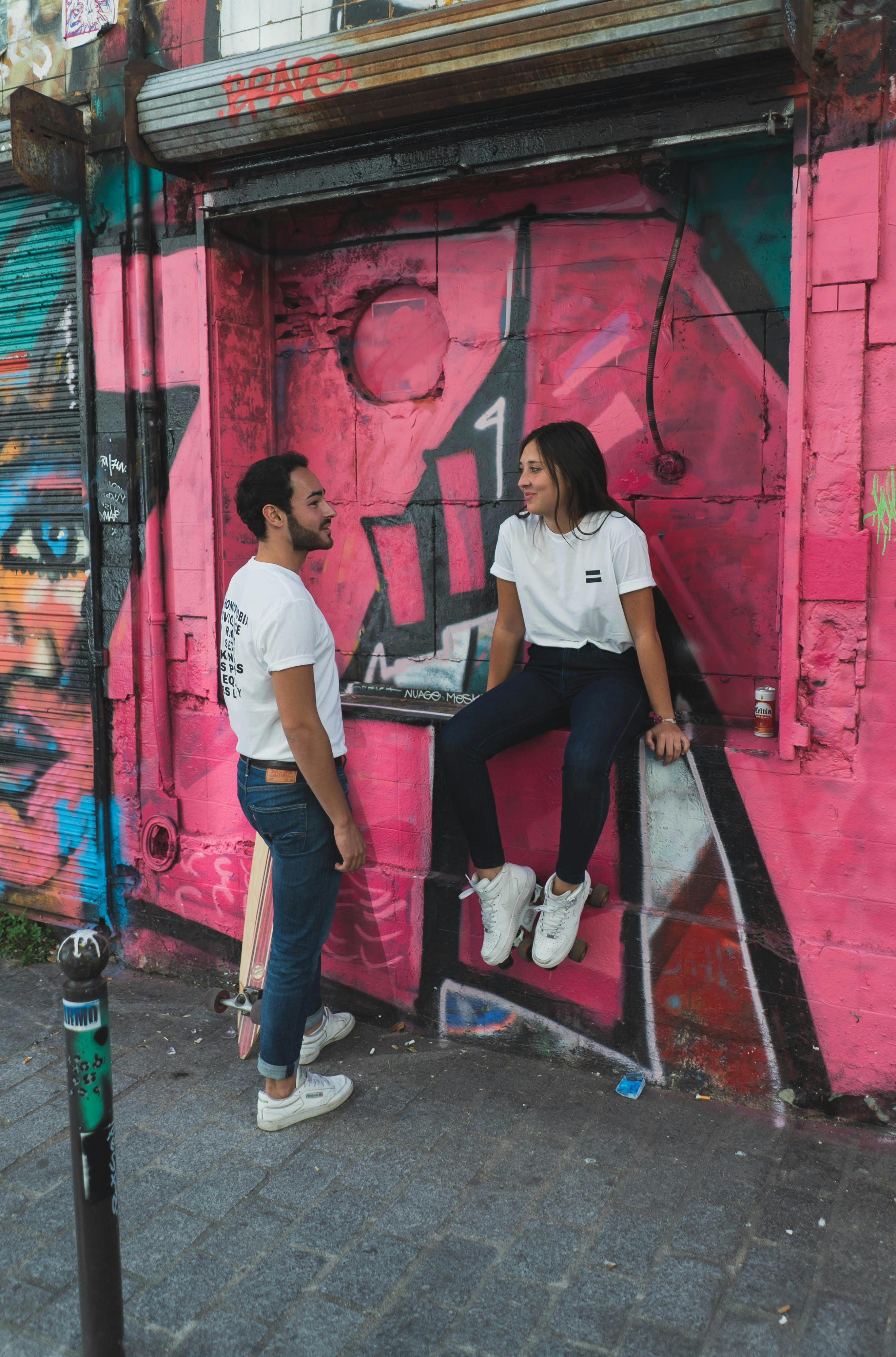 Two artist friends sharing a creative moment in front of a vibrant graffiti-covered wall, highlighting their connection through artistic expression and mutual inspiration. 