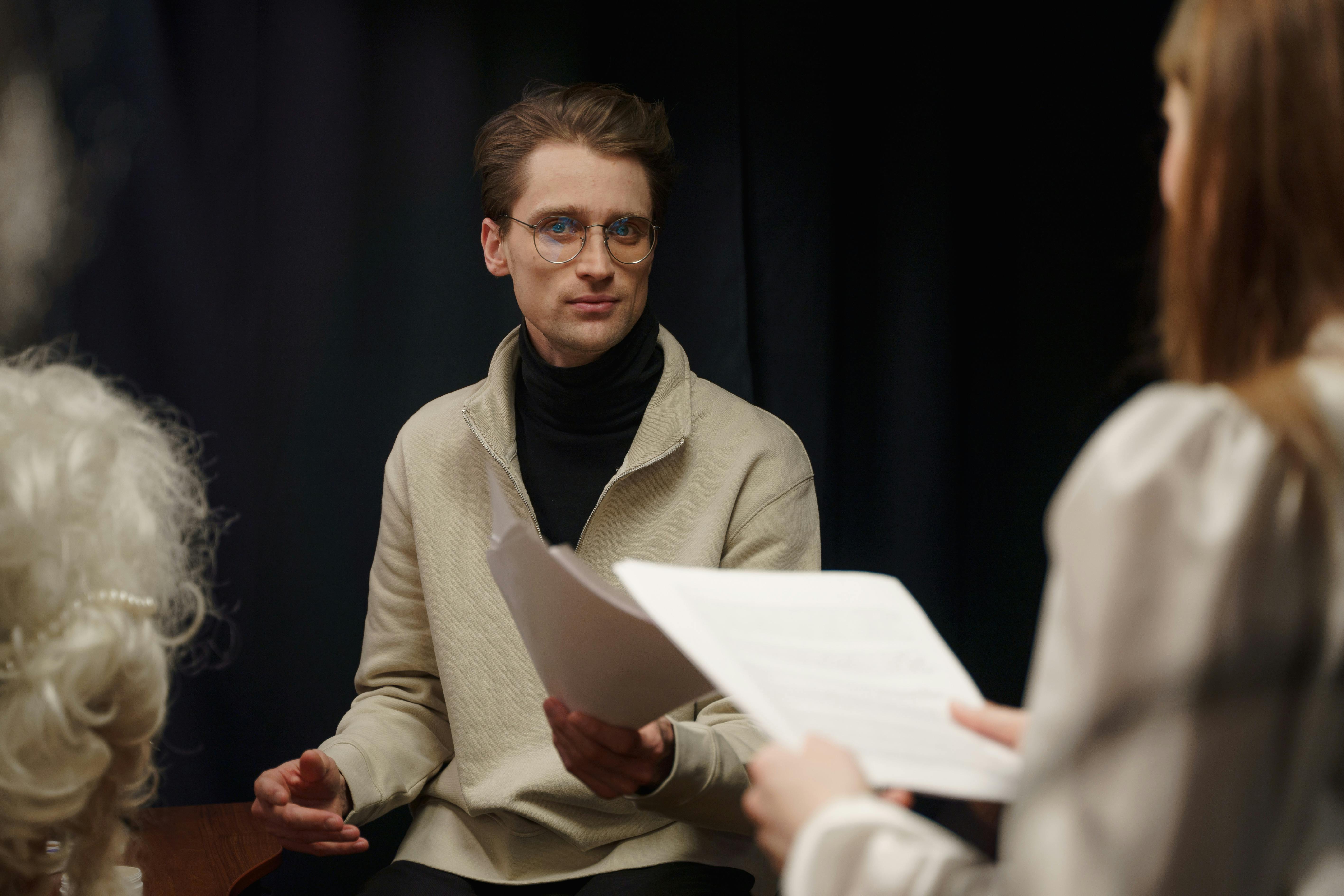 Two people holding scripts and practicing a scene together in a dimly lit room, symbolizing collaboration and connection during an improv or acting session.