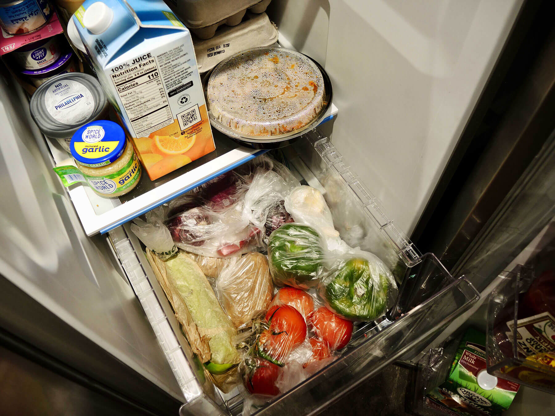 The insides of a fridge, packed full with produce and leftovers.