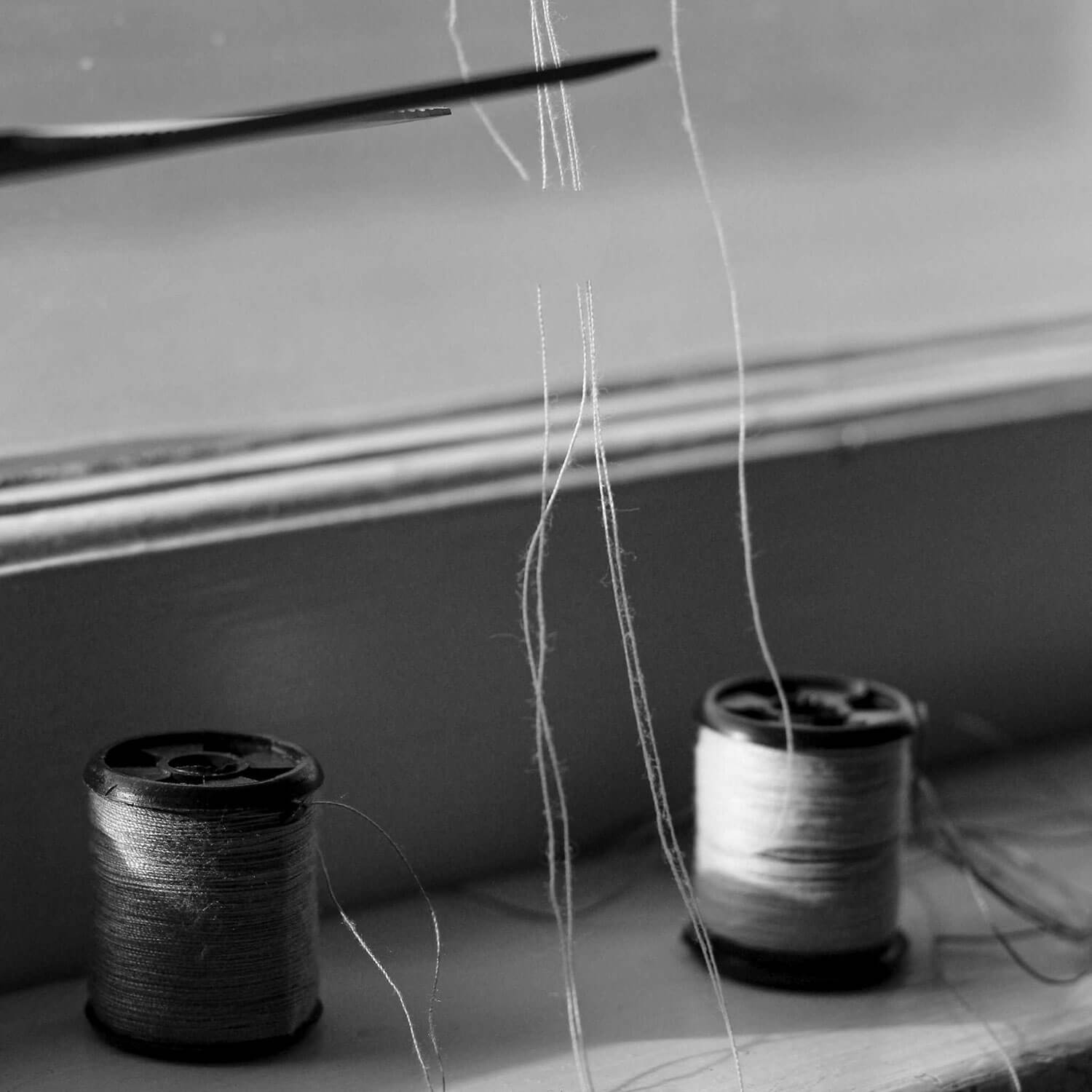 A black and white photo of two spools of thread — they're tangled, but a pair of scissors is cutting them off at the top.
