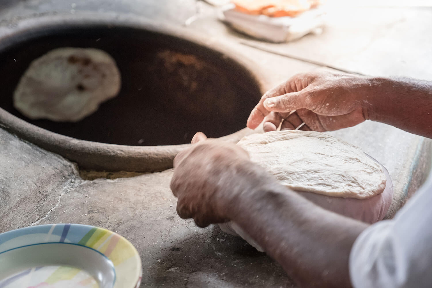 Flat bread is baked in a round clay oven.