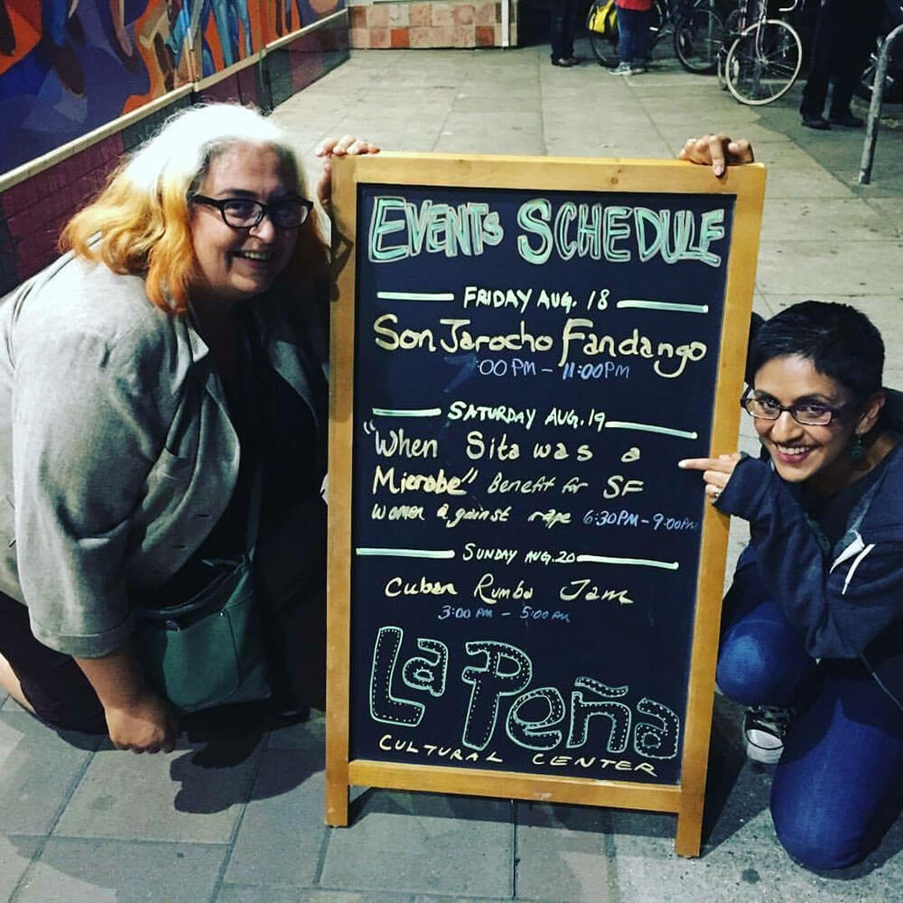 Sandhya Jha and Tuhina Verma Rasche together in front of a sign at La Peña Cultural Center