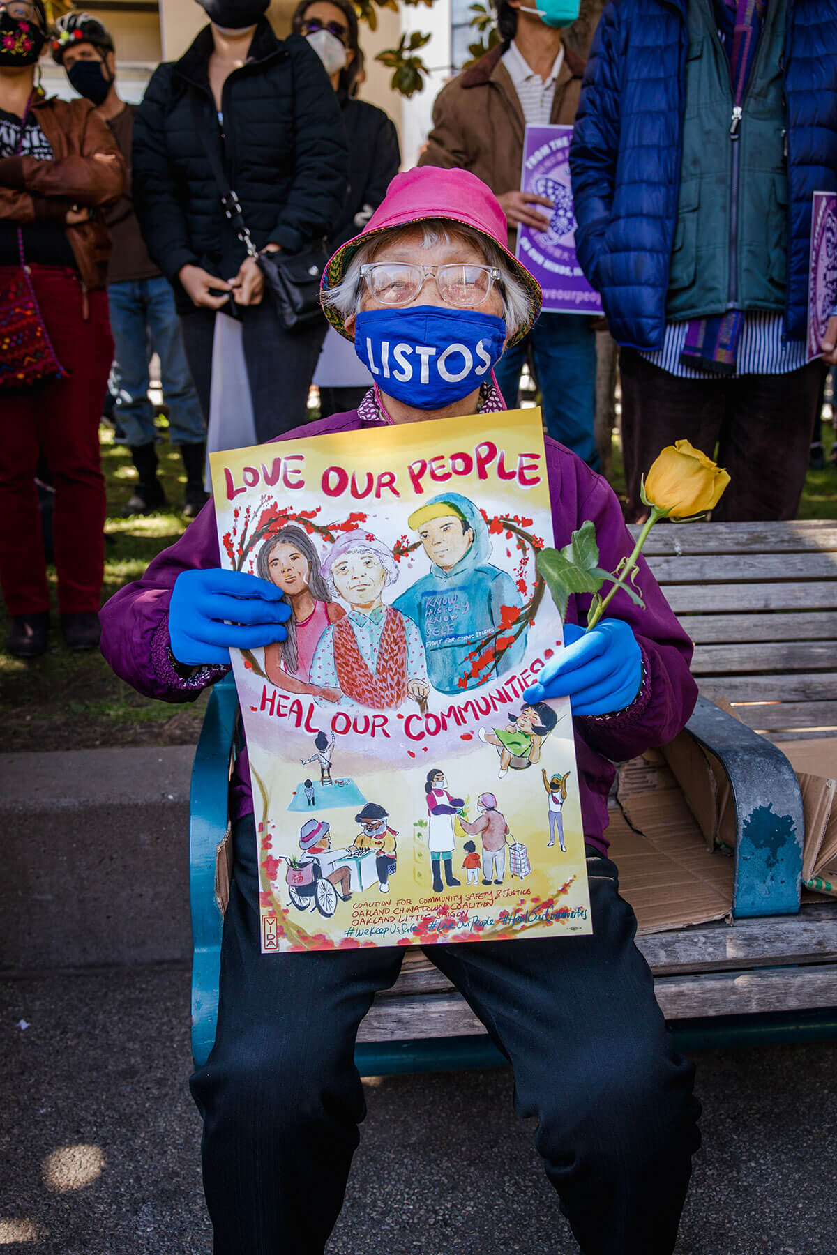 Older Asian woman holding a sign that says "Love Our People, Heal Our Communities" at a Stop Asian Hate protest
