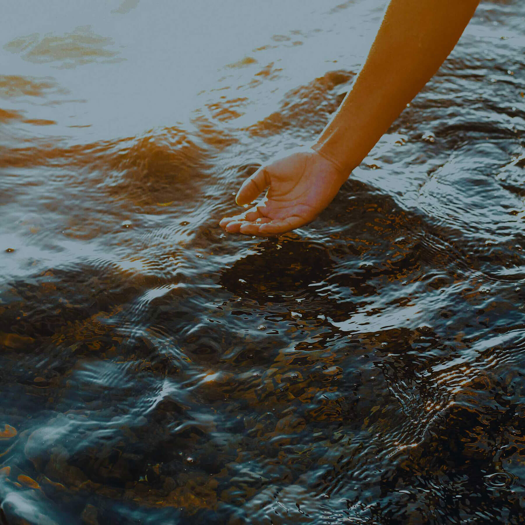 The back of a hand caresses a stream of moving water. 