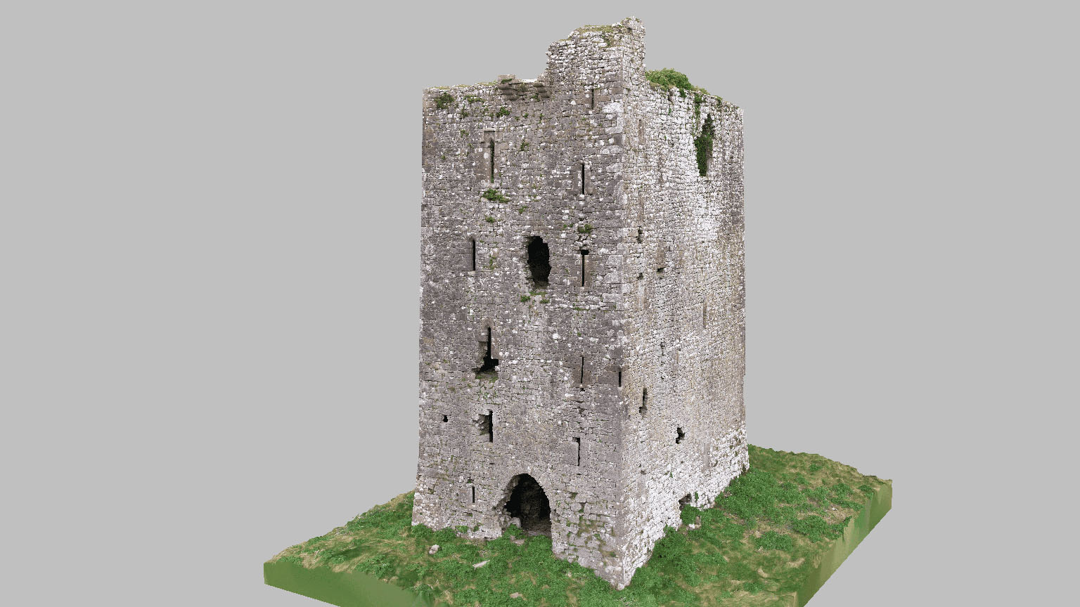 Ruined medieval stone castle tower with small windows and an arch entrance on a grassy base.