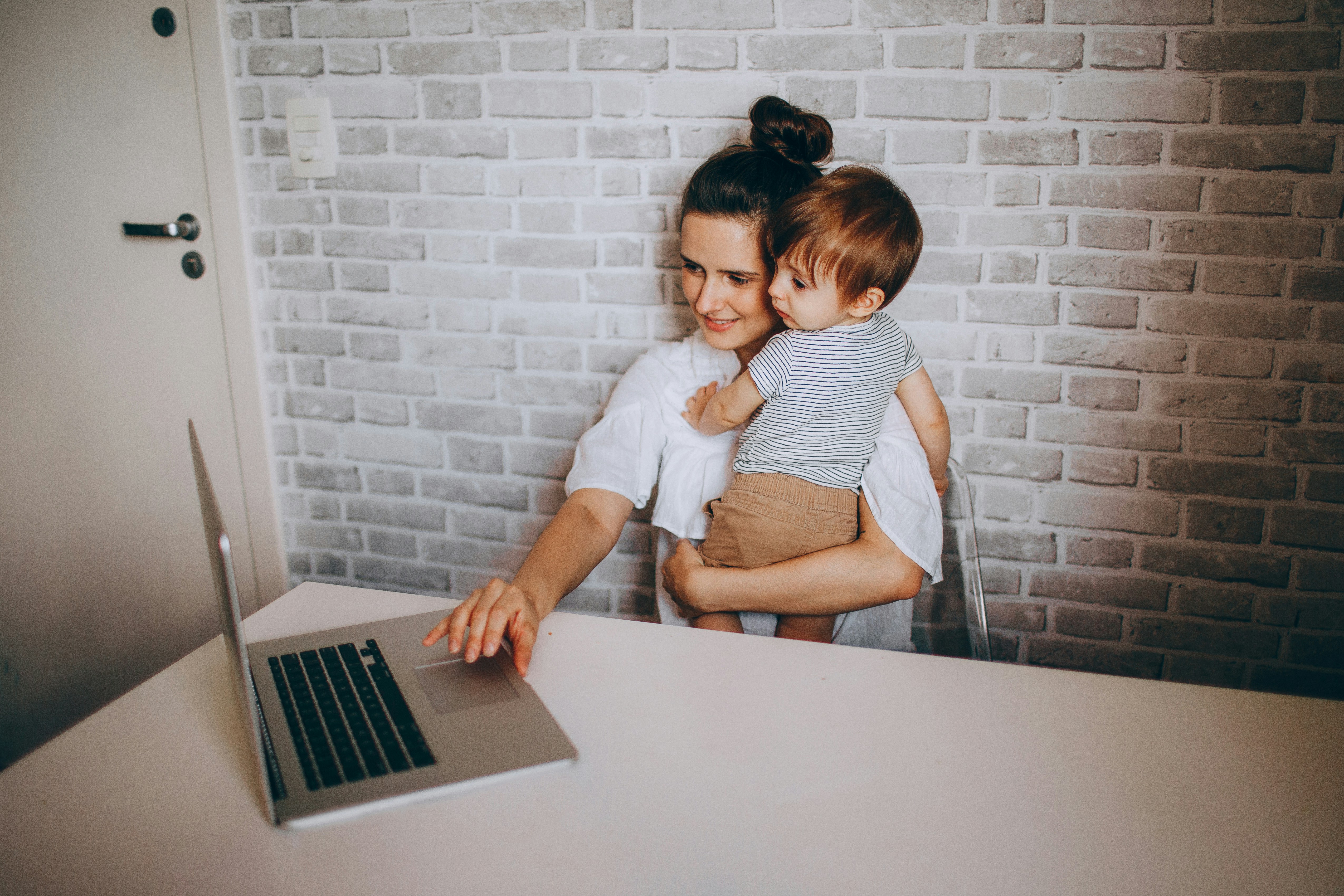 A woman holding a child with a laptop working in front of her