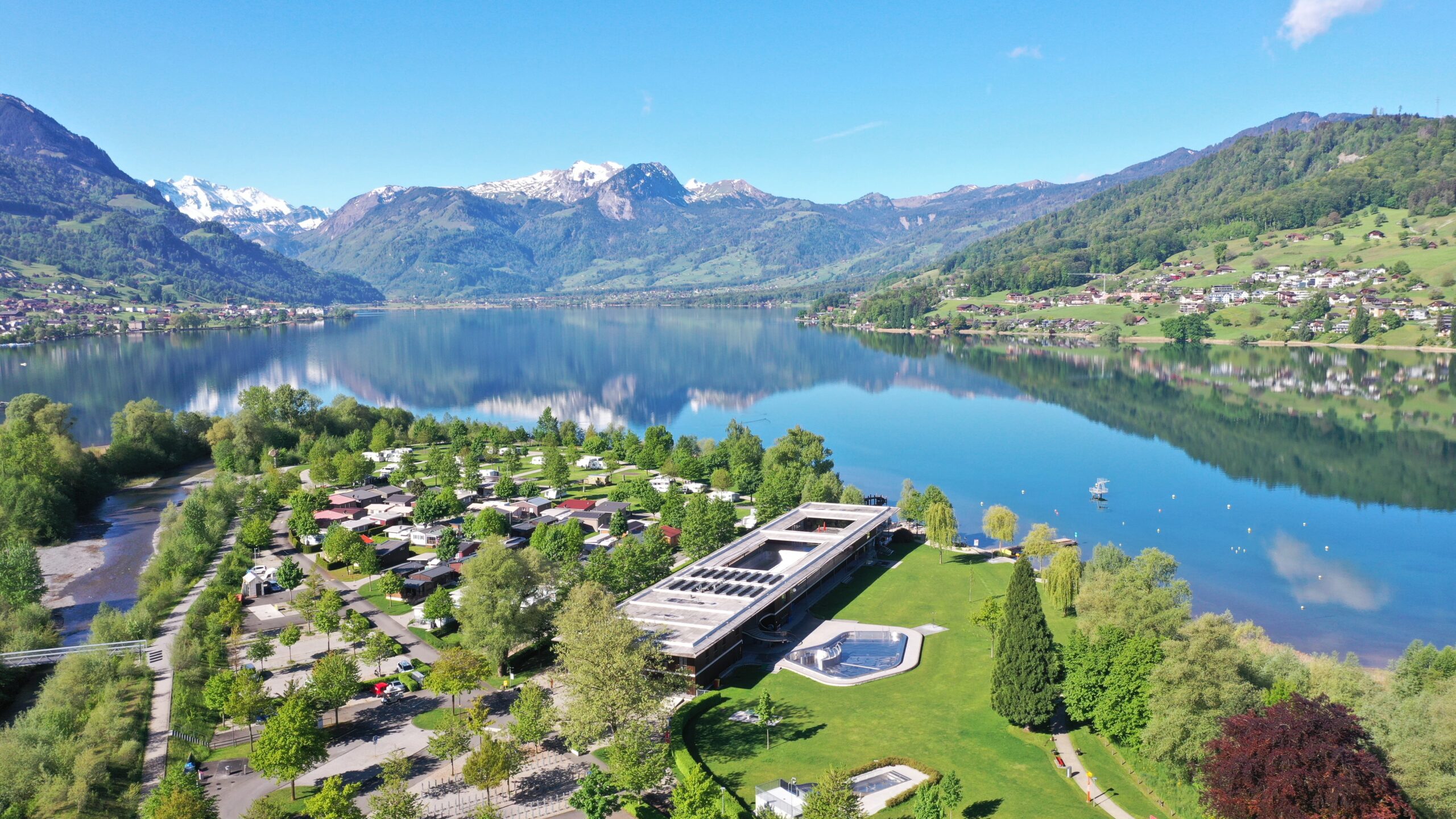 Grosser Wohnmobil-Liner auf einem Stellplatz am Sarnersee, im Hintergrund alpine Bergkulisse mit weissen Gipfeln, ruhige Stimmung bei Sonnenlicht