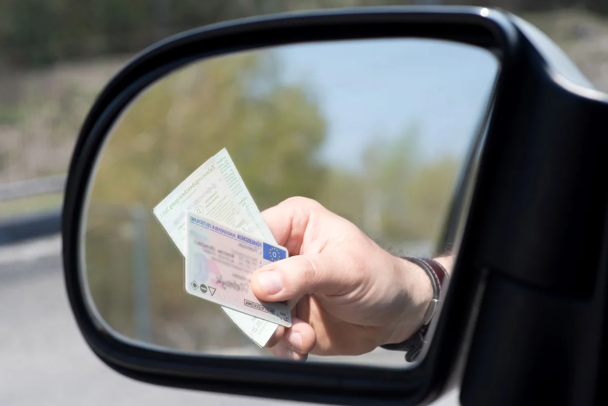Hand mit Dokumenten im Rückspiegel eines Fahrzeugs
