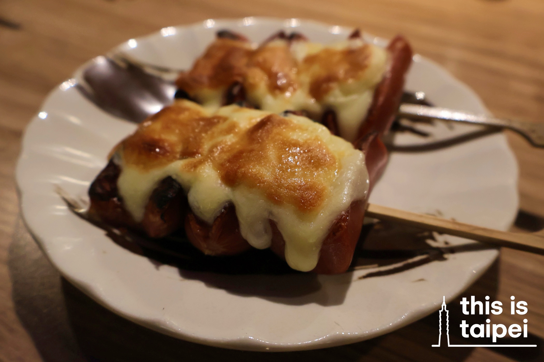 Portions of sausages topped with melted cheese and salted egg yolk water lily shoots from Fengfu Izakaya in Zhongshan District. (Photos by KB, January 2026 / © This Is Taipei)