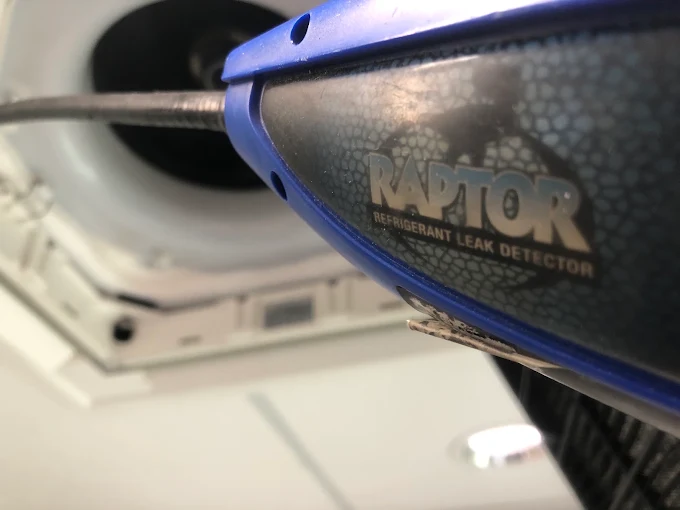 Refrigerant leak detector being used to check a ceiling-mounted air conditioning unit.