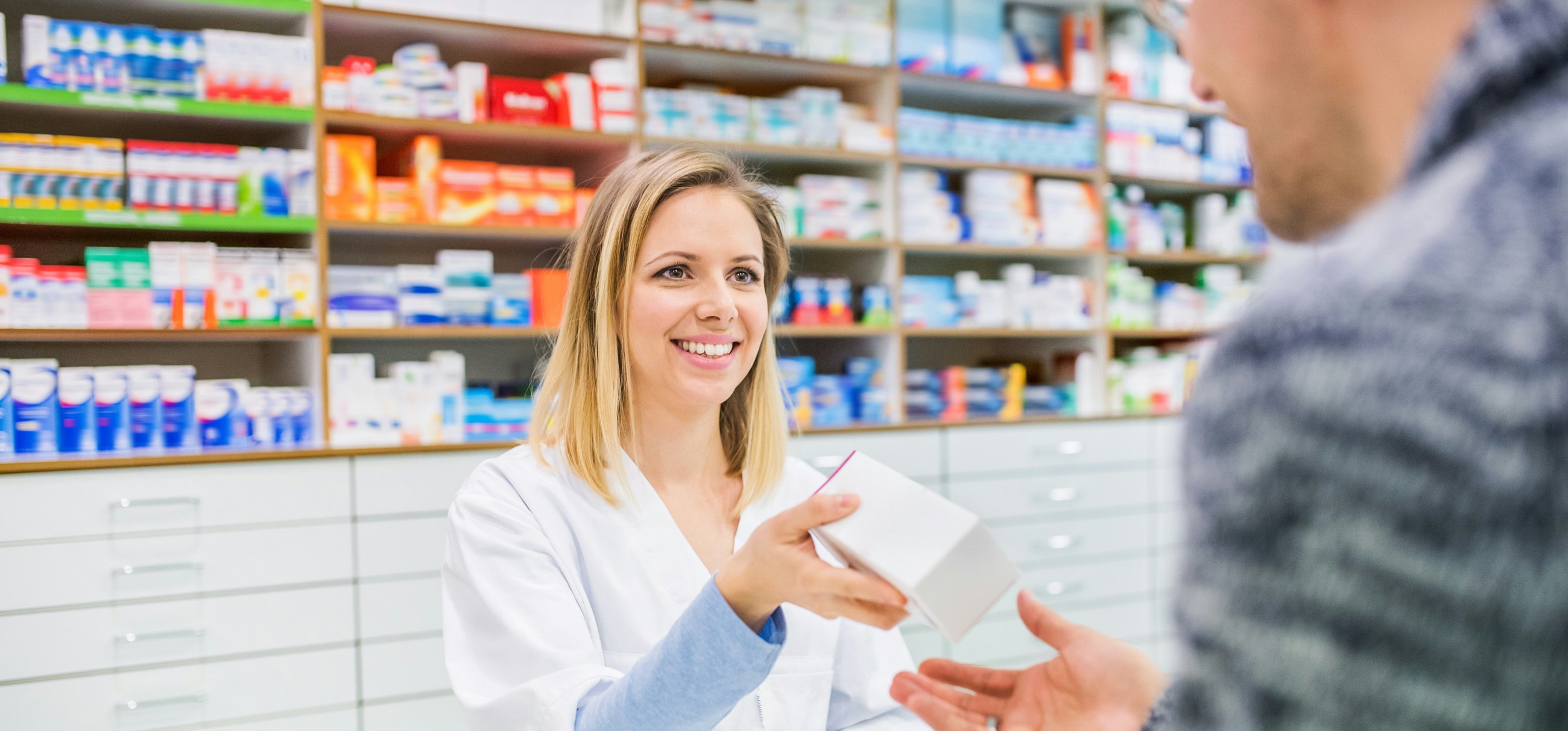 Ein Apotheker, der einem Kunden eine Medikamentenschachtel über den Tresen reicht