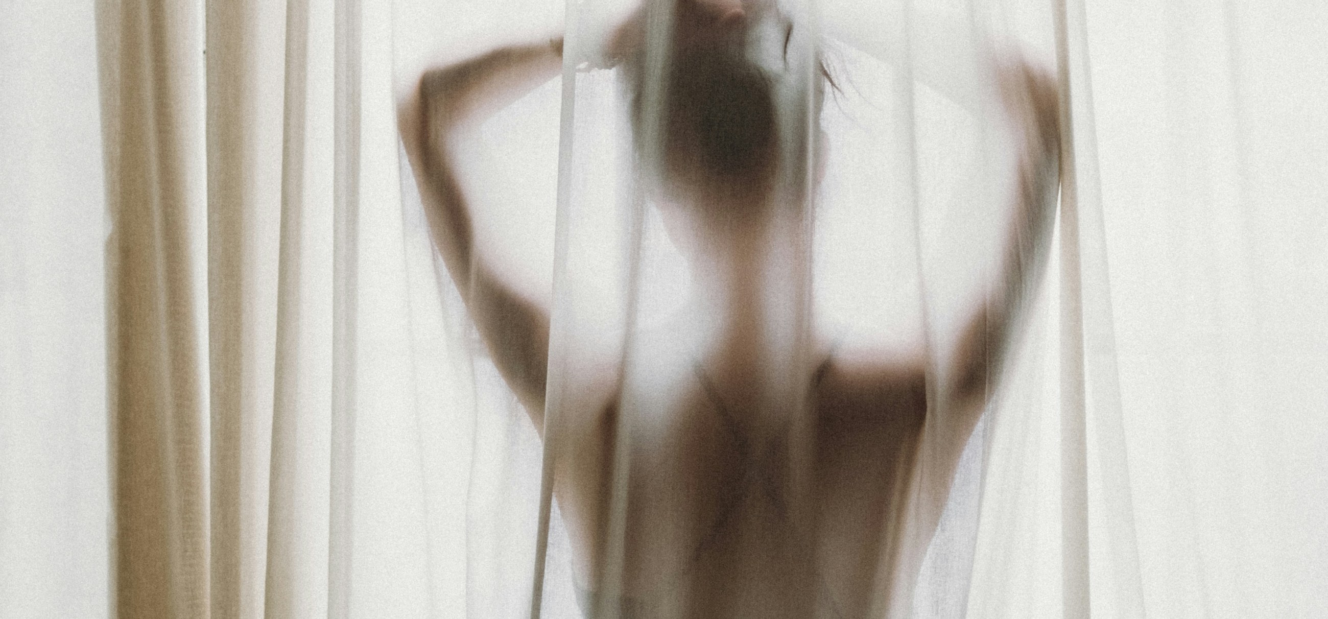 A person stretching behind a sunlit curtain