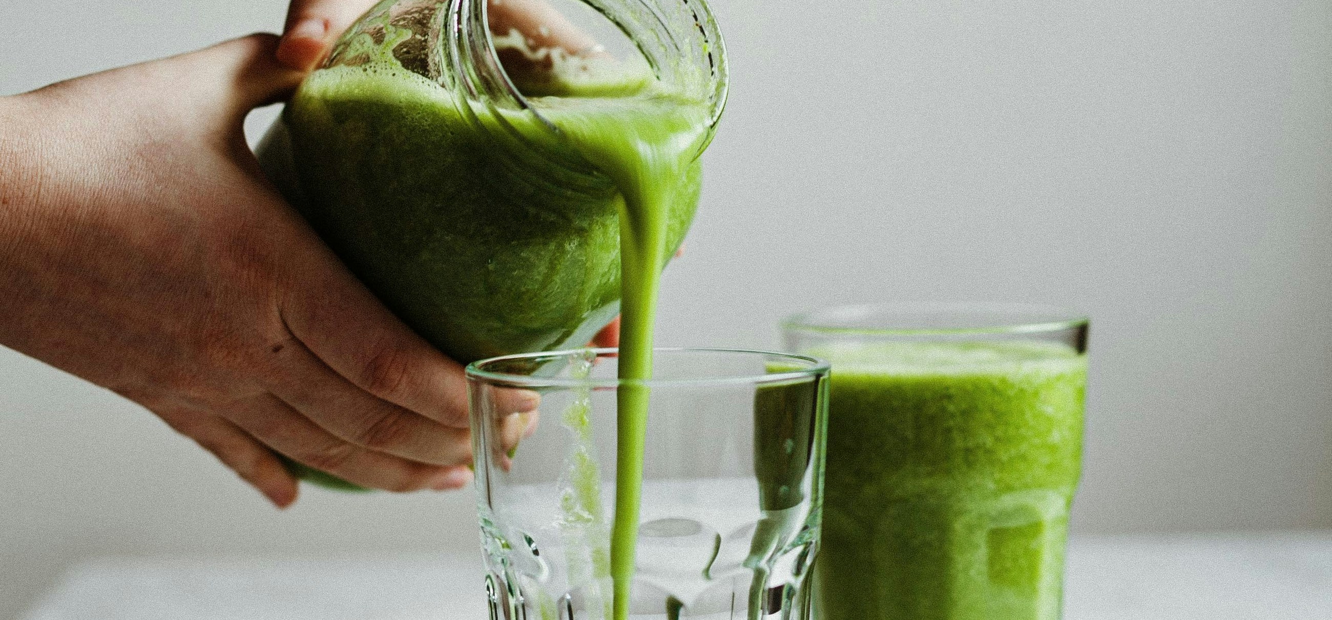 Green juice being poured from a jar into two glasses