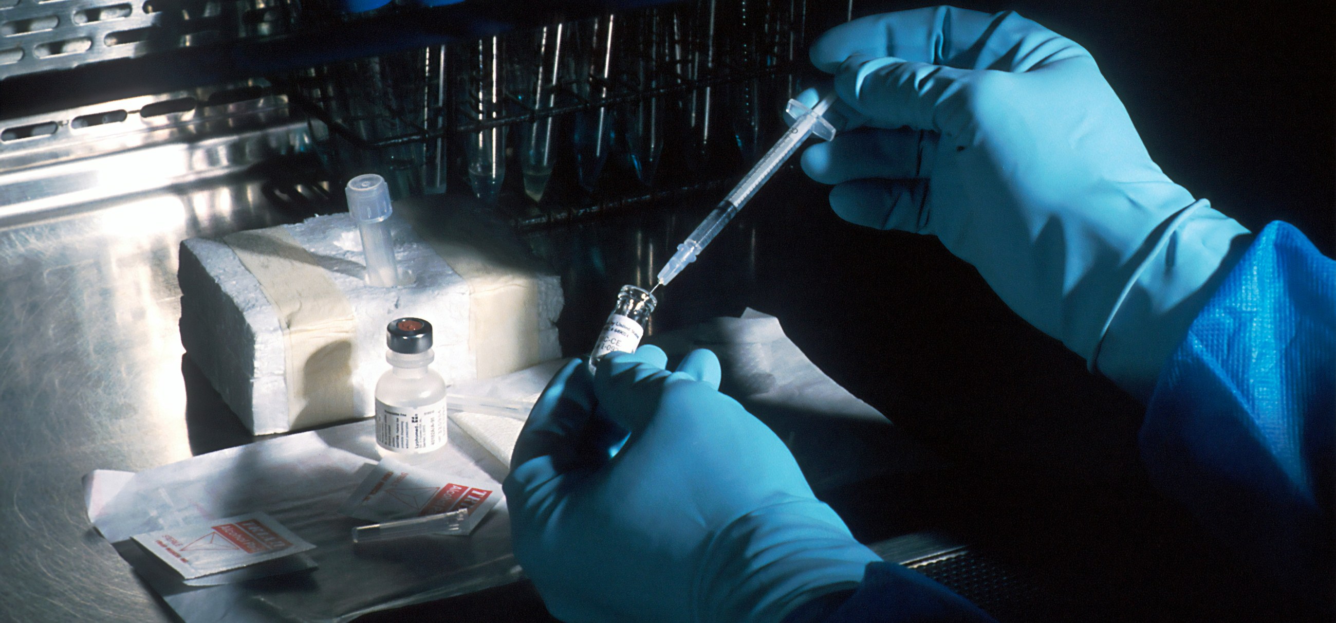 Gloved hands drawing a sample into a syringe in a laboratory