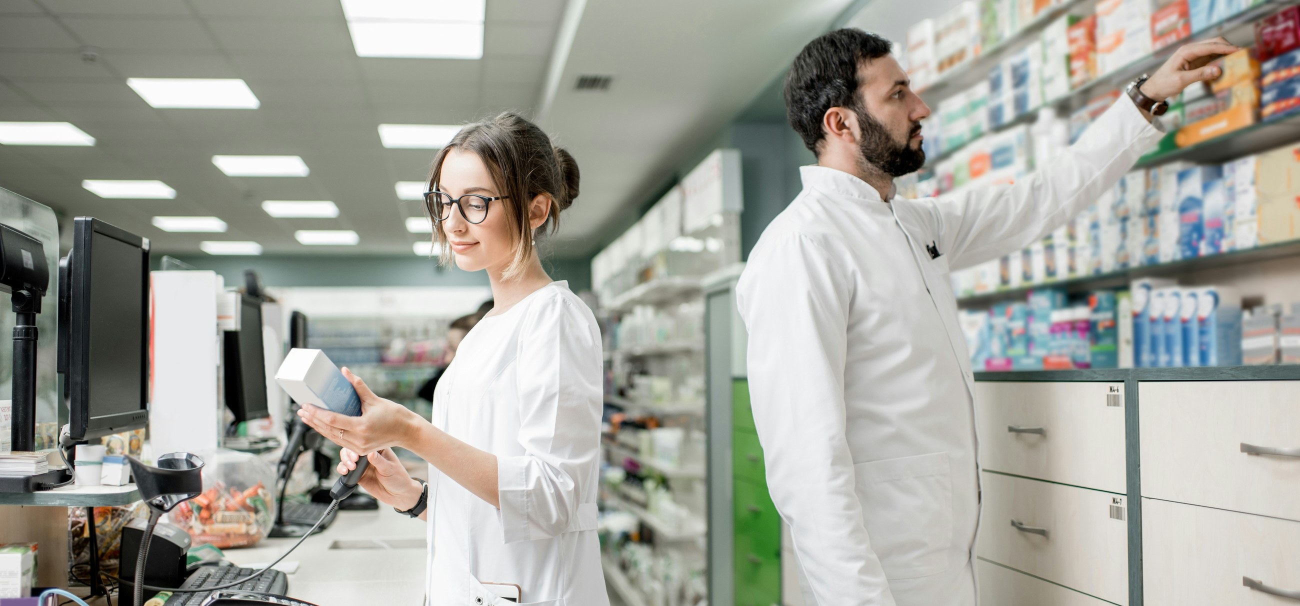 Two pharmacists work side by side behind the counter of a German pharmacy