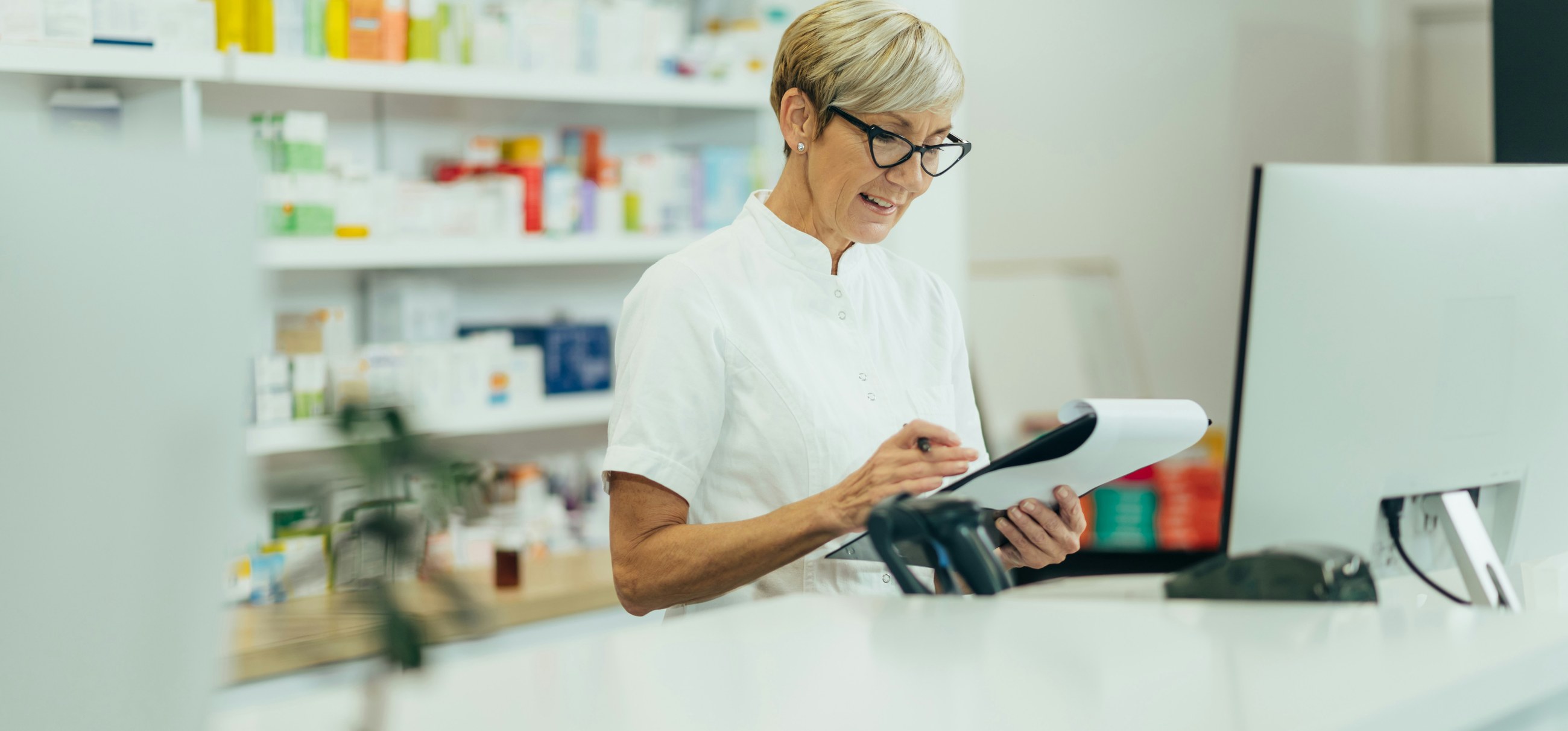 A pharmacist fills in a form on a clipboard at the pharmacy counter