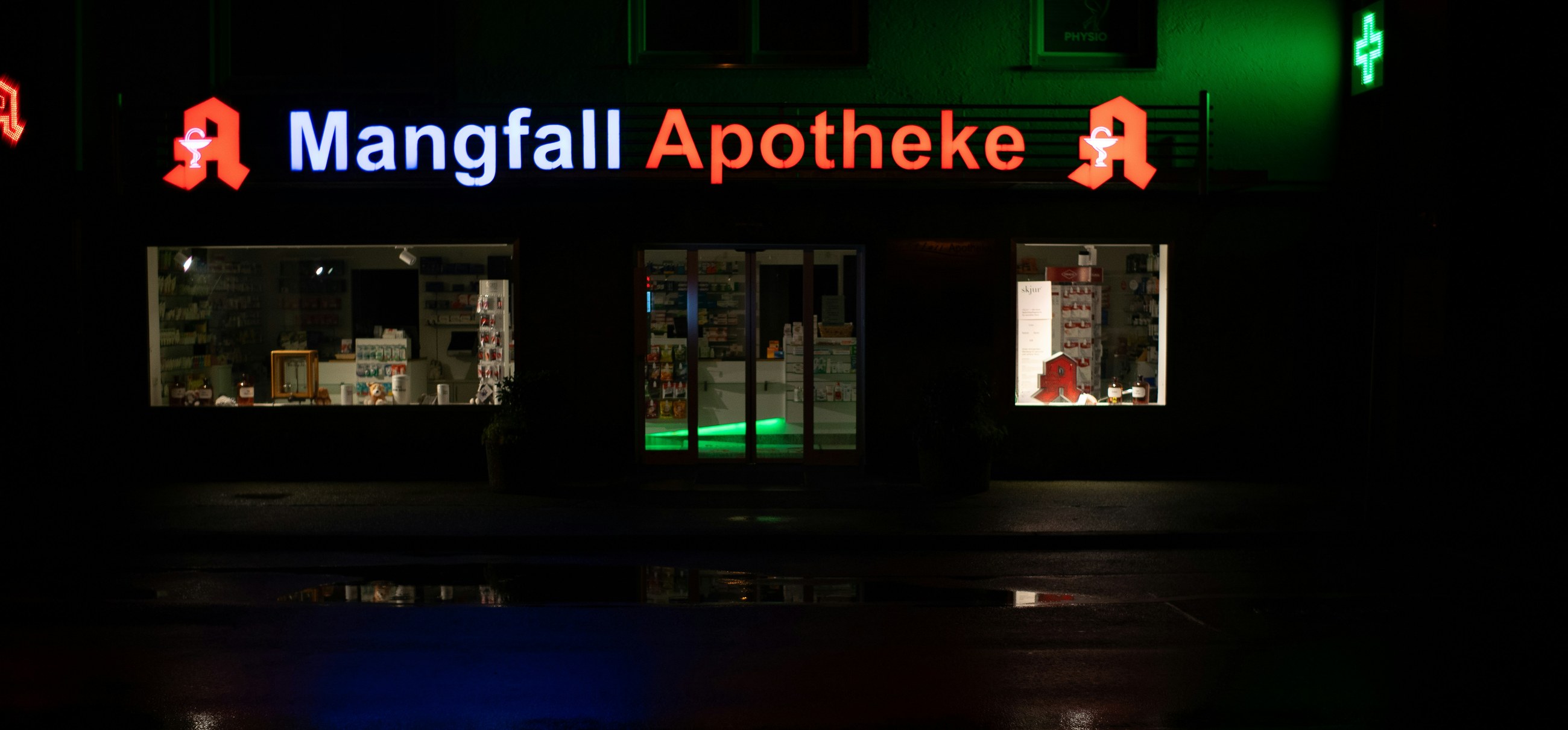 A German pharmacy sign glows above the shop window at night