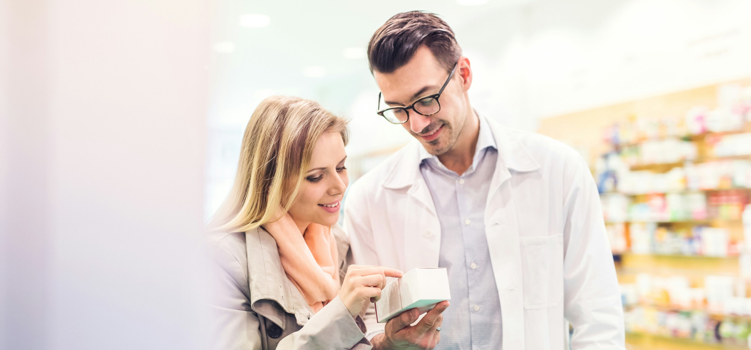 A pharmacist and a customer look at a package together in a quiet corner of the pharmacy