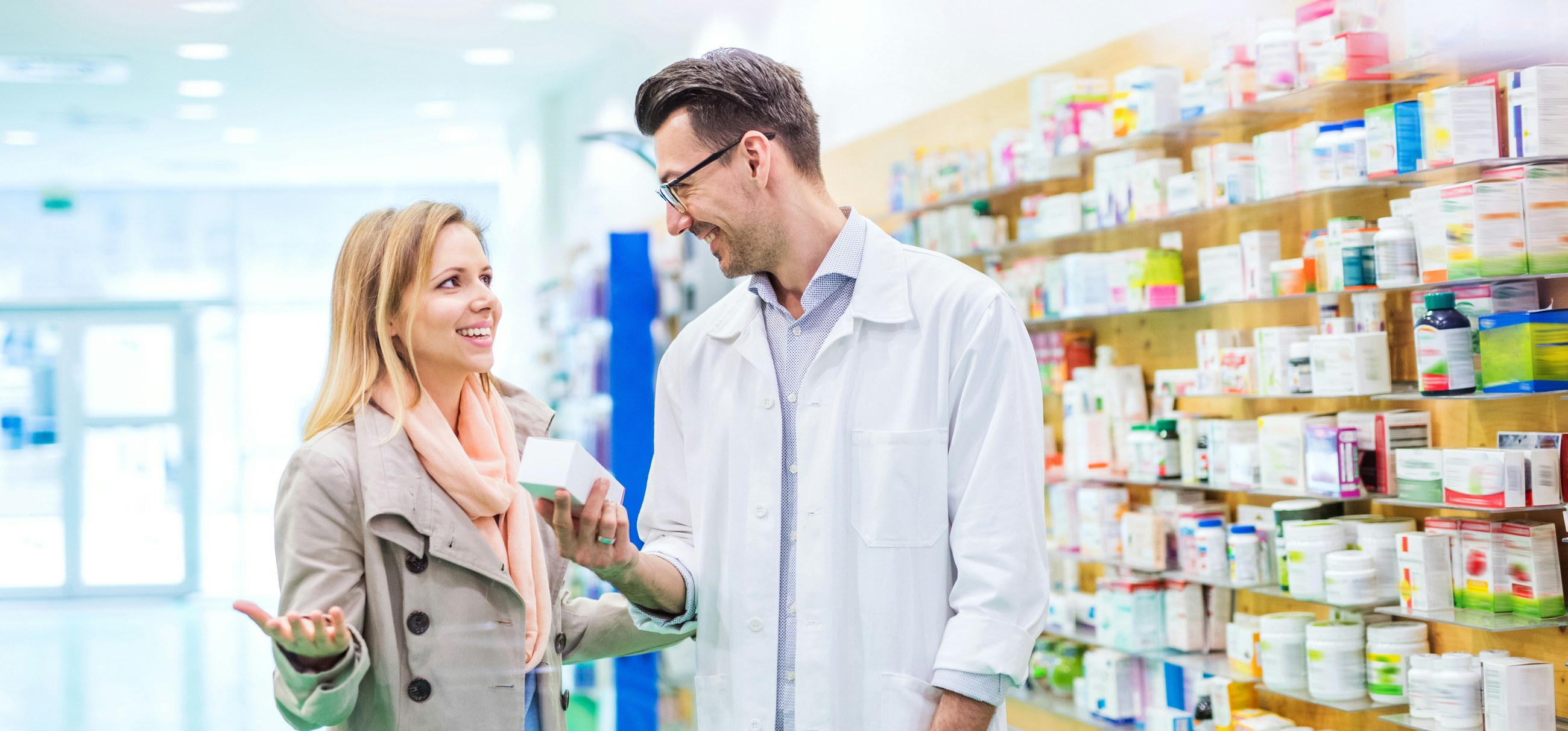 A pharmacist advises a customer in front of the pharmacy shelves