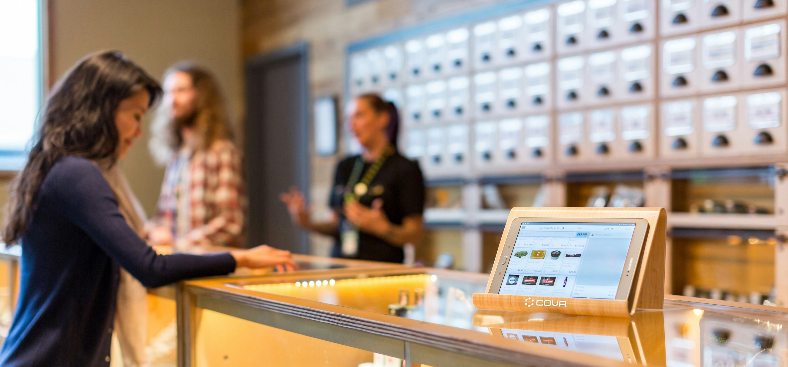 A tablet stands on the counter while staff serve customers in the background