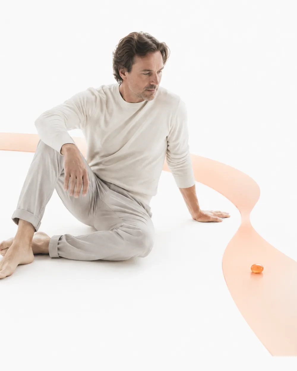 A man seated beside a winding orange path with one orange bead resting on it, the image for the Aniva homocysteine test.