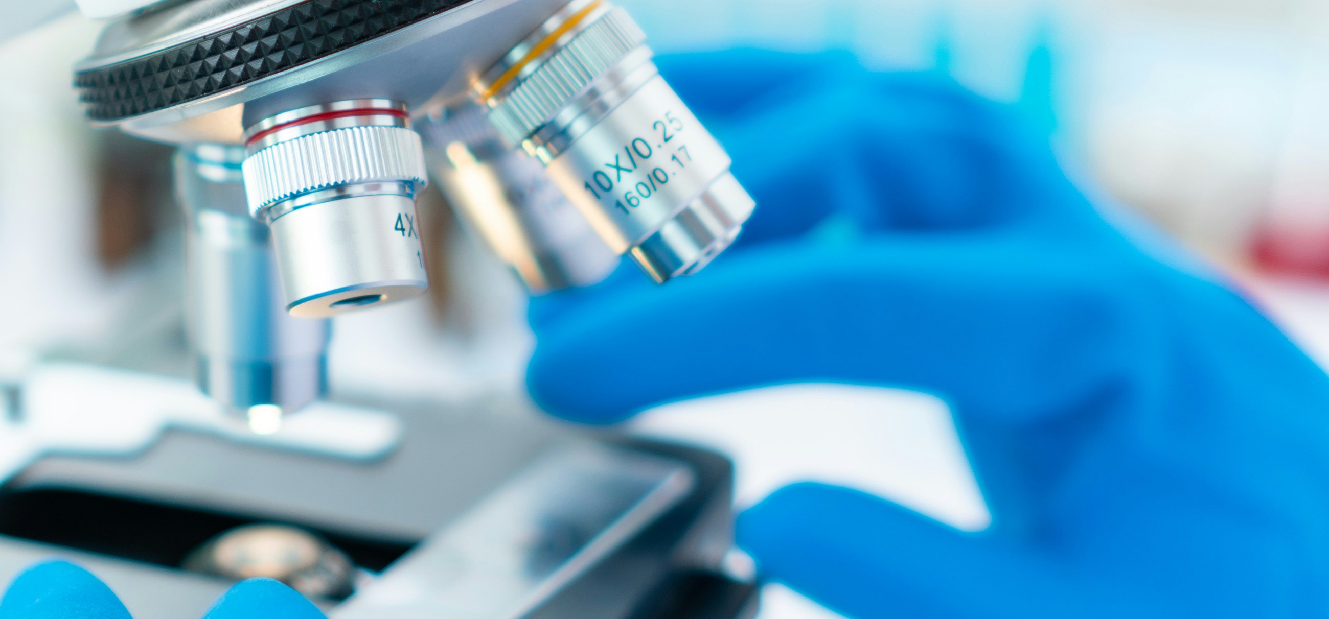 A close view of microscope objective lenses being adjusted by a gloved hand
