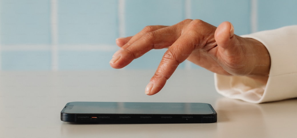 A hand reaching towards a smartphone on a pale surface