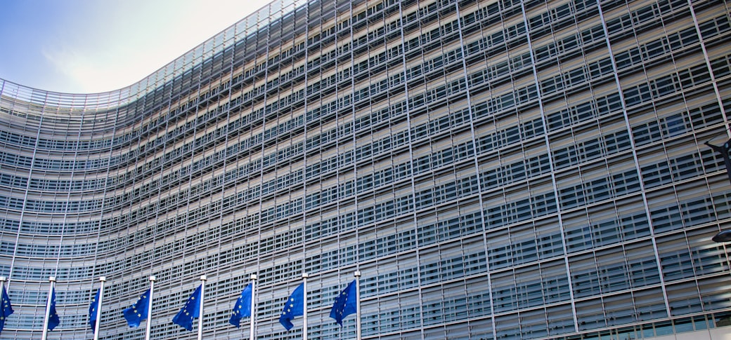 A curved glass building above a row of small European flags