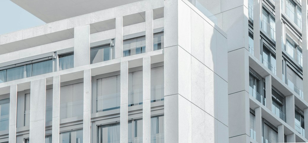 The corner of a pale stone-clad contemporary building with deep vertical fins and full-height glazing against a clear sky.