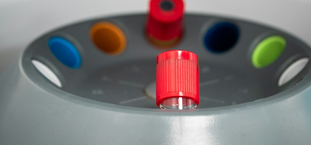 A close view into a centrifuge rotor with a single red-capped tube seated in one of the coloured positions.