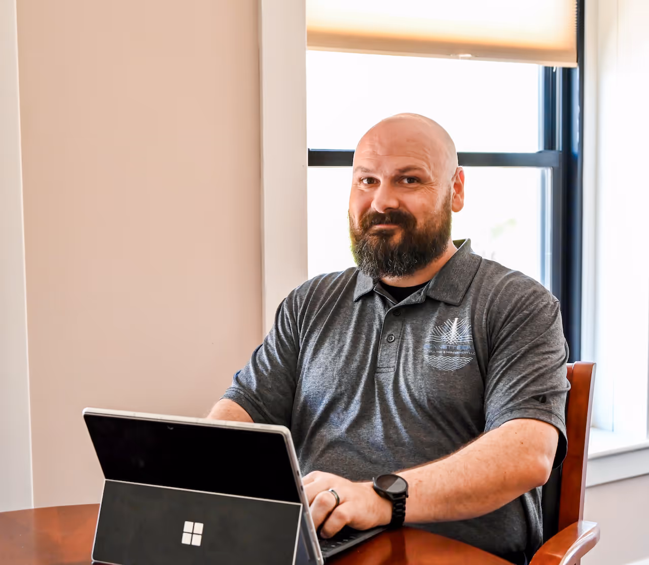 A bald man with a dark beard smiles at the camera over a laptop.