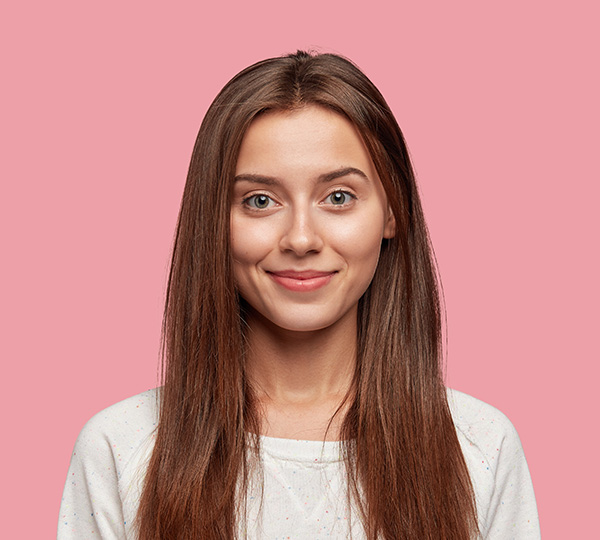 Woman with long brown hair smiling against pink background