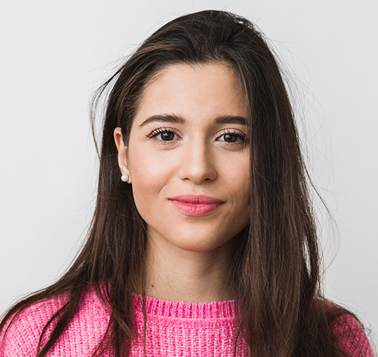 Young woman in pink sweater smiling softly against neutral background