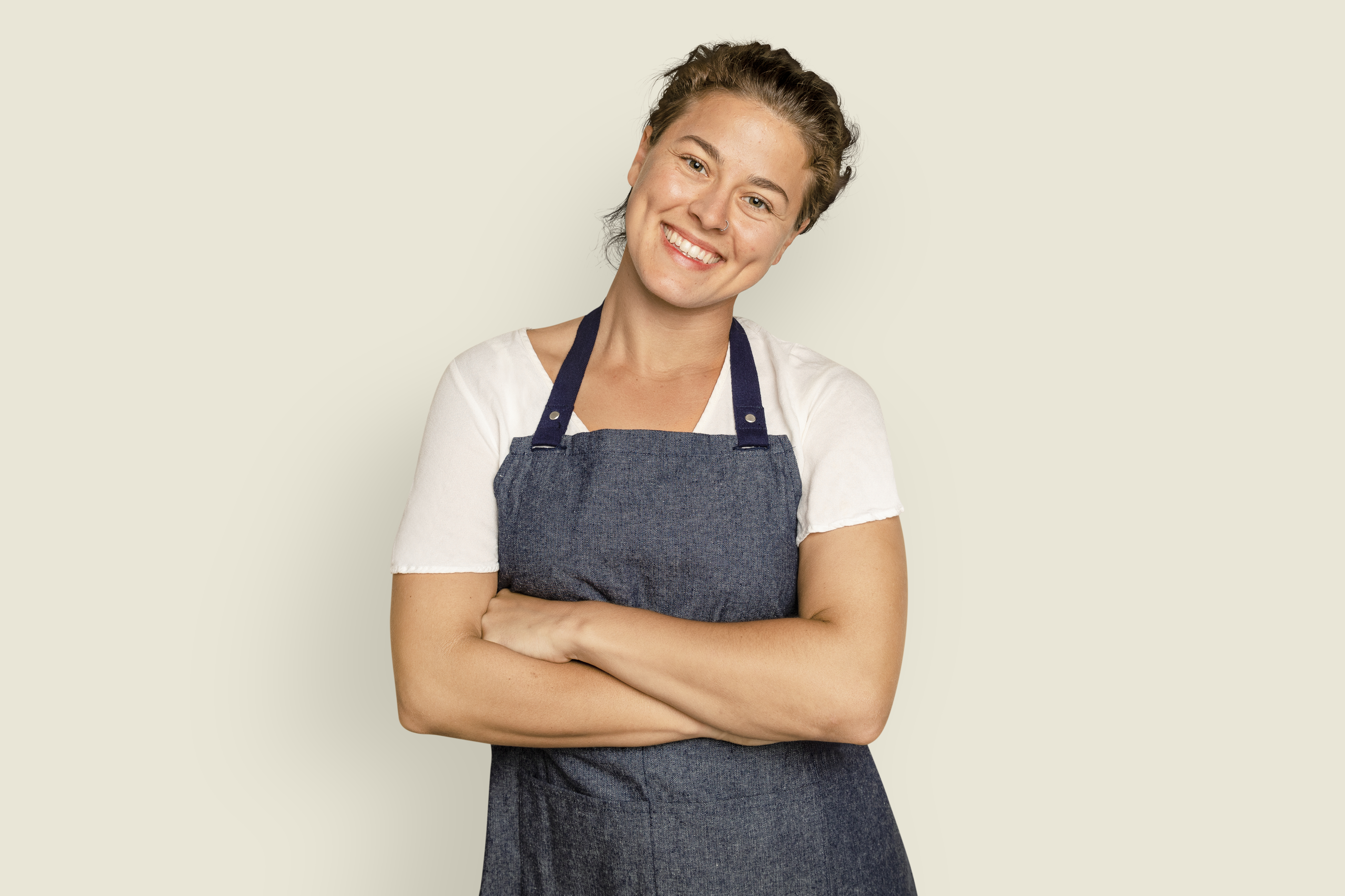 Smiling chef in denim apron with crossed arms against plain background