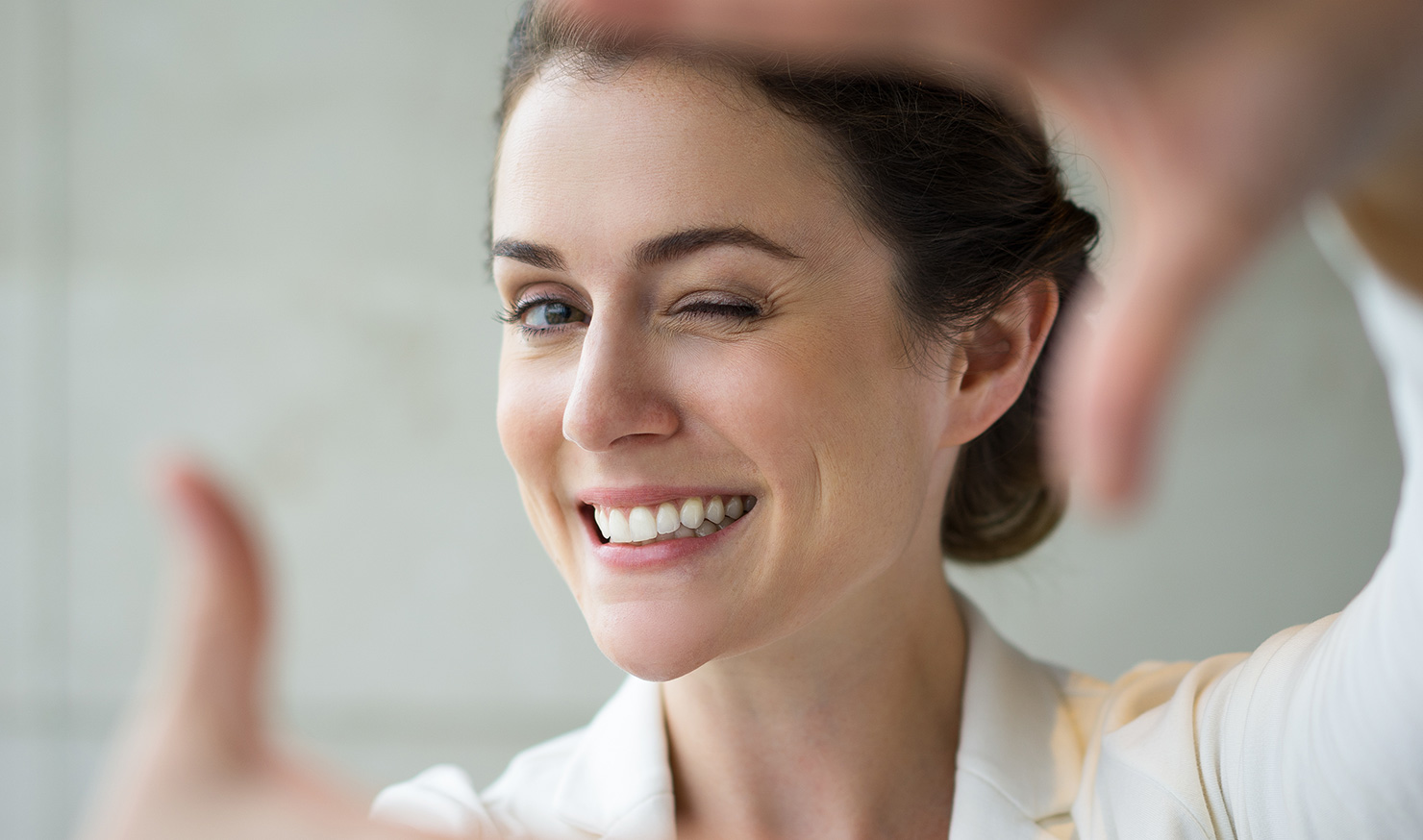 Smiling woman winking, wearing white blazer, soft background