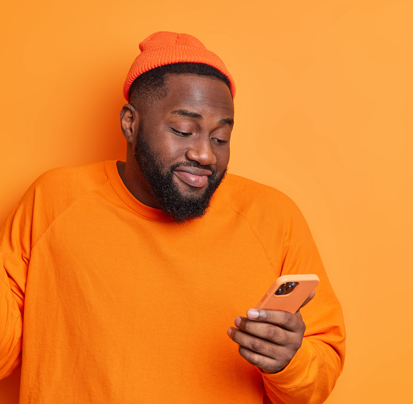 Person in orange outfit looking at phone against bright orange background