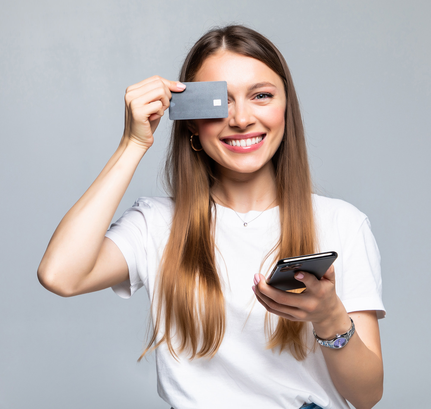 Smiling woman holding credit card and smartphone against gray background