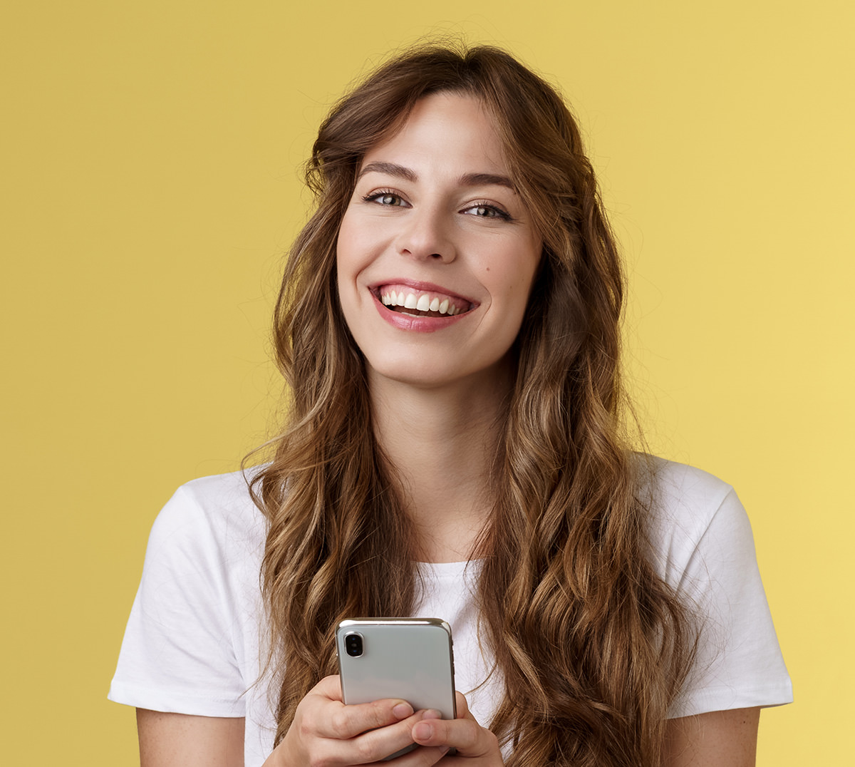 Smiling woman in white shirt holding smartphone against yellow background