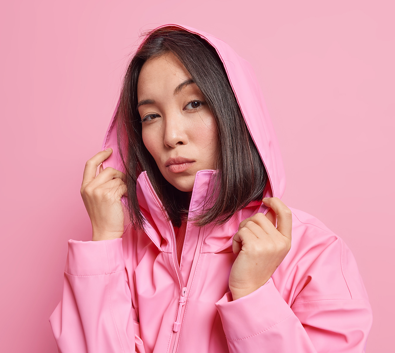 Woman in pink hoodie looking serious against matching pink background