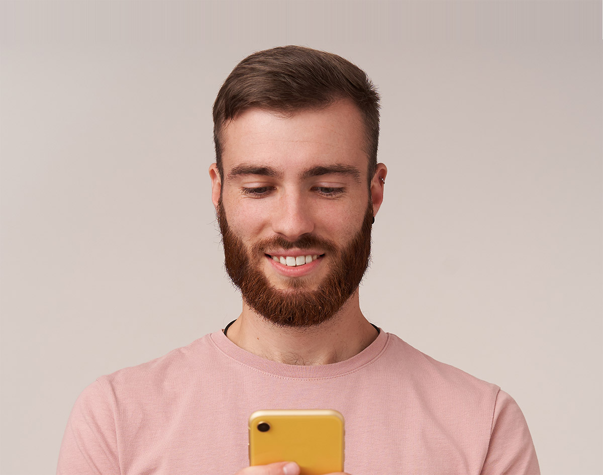 Smiling person in pink shirt looking down at yellow smartphone