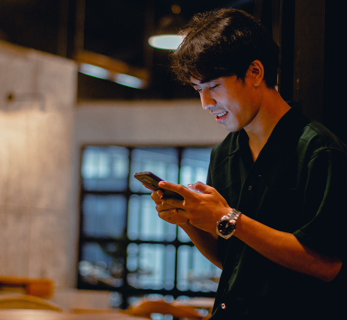 Person smiling while using smartphone in dimly lit interior space