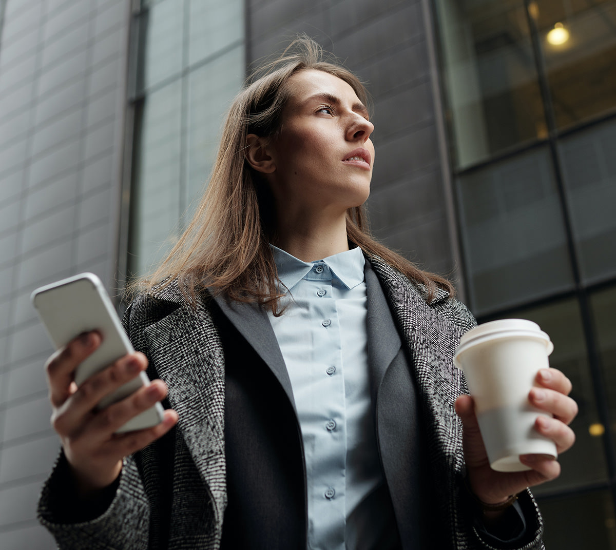 Professional woman with coffee and phone near modern office building