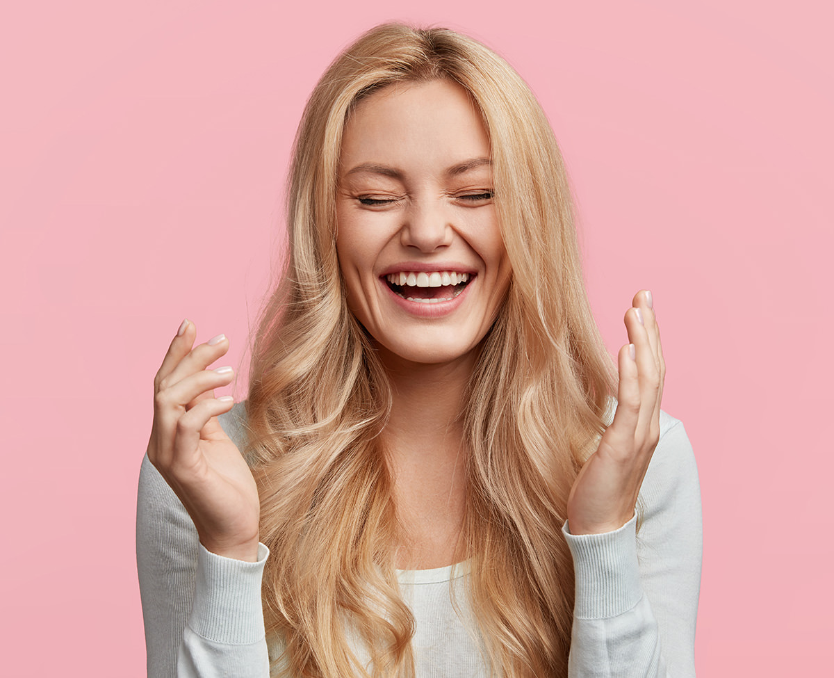 Blonde woman laughing joyfully with closed eyes against pink background